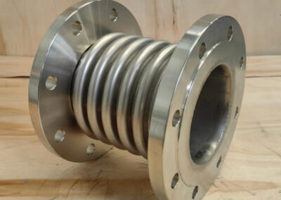 Metallic pipe expansion joint on wooden surface.
